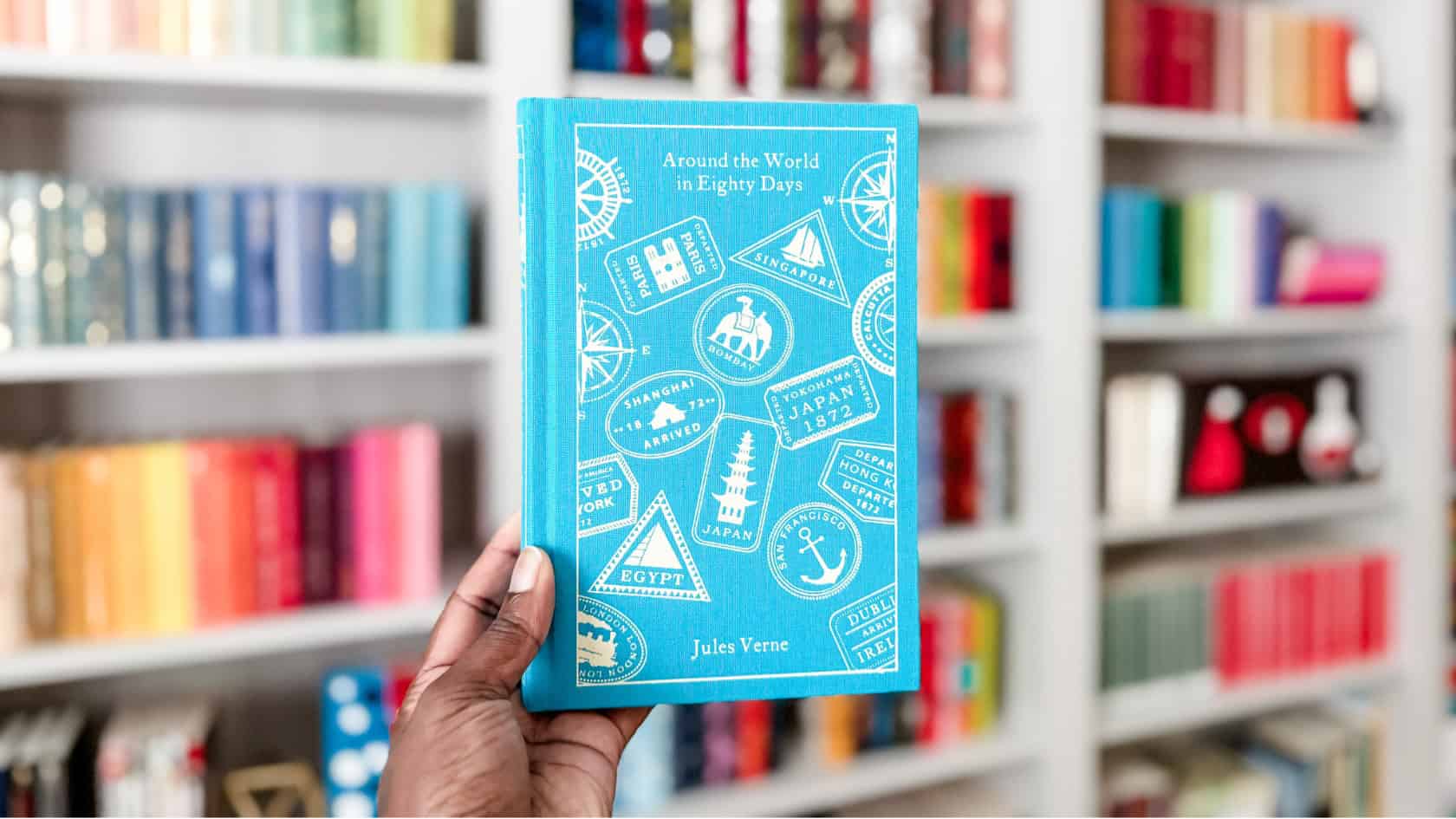 Holding a copy of the penguin clothbound edition of Around the World in Eighty days with my bookshelves in the background