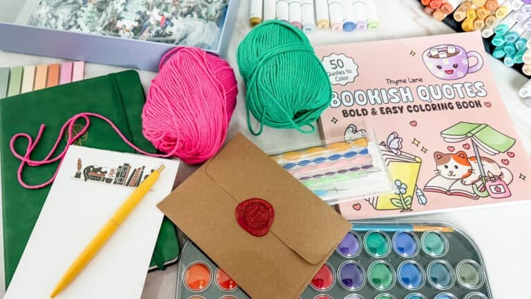 low-cost relaxing hobbies arranged on a cozy table at home with adult coloring supplies, journal, puzzles, yarn, paint, letter writing