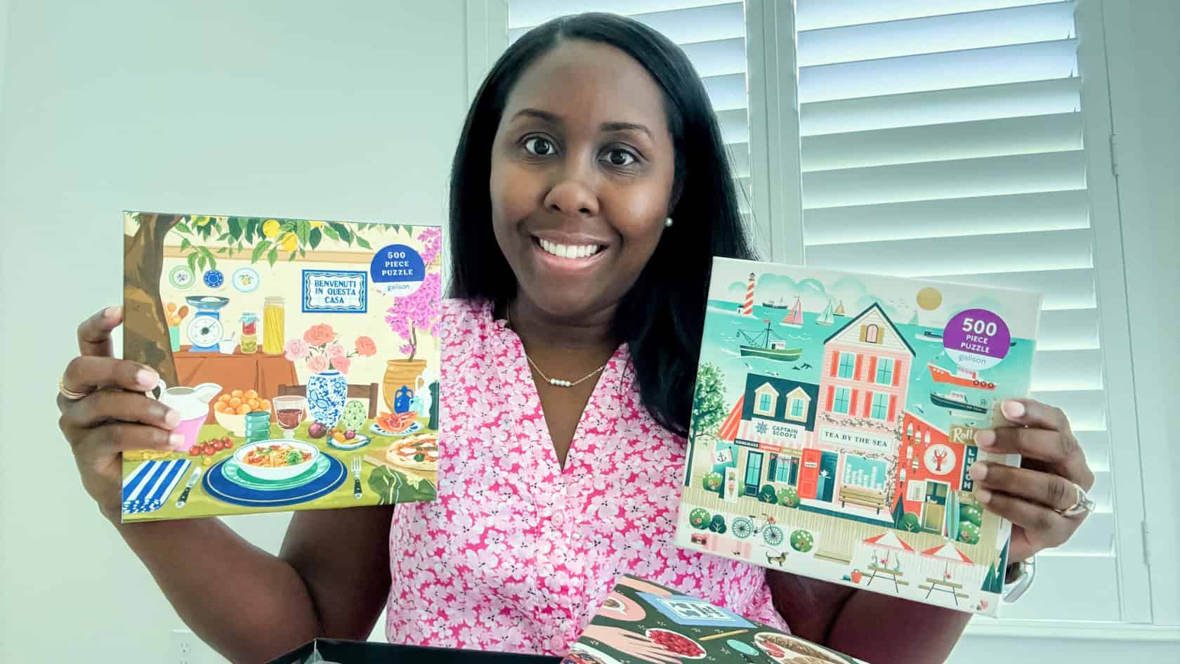 Victoria (Me) holding two summer jigsaw puzzles, one in each hand, with one puzzle on the table open