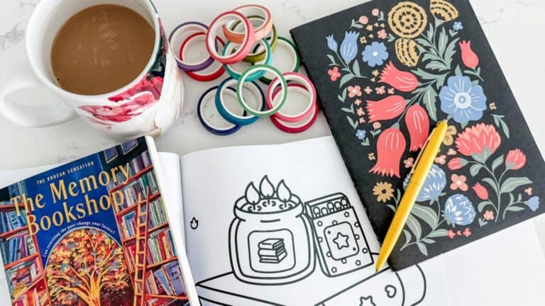 my soft week menu cozy setup with my coffee, coloring pages, journal, wash tape and the memory bookshop book