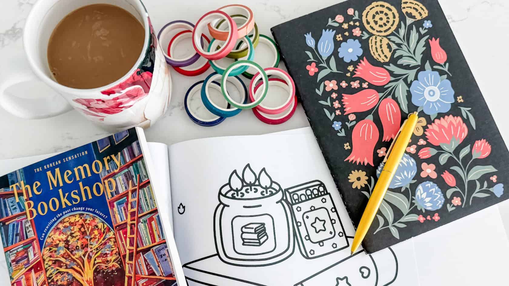 my soft week menu cozy setup with my coffee, coloring pages, journal, wash tape and the memory bookshop book